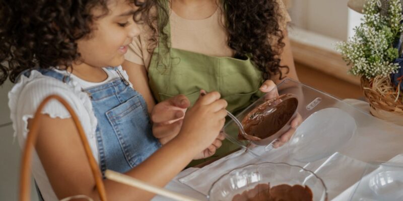 Mãe e filha preparando chocolate caseiro. Representação do impacto da ciência e tecnologia alimentar na criação de produtos mais saudáveis, incluindo lipídios de baixa absorção.